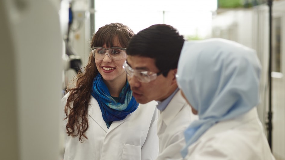 Photo of three people wearing lab coats and safety goggles.